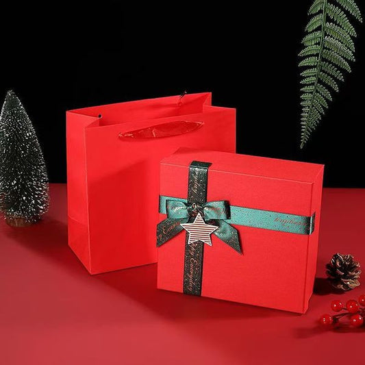 Red gift box with a green ribbon and star detail next to a matching red paper bag, set against a dark background.
